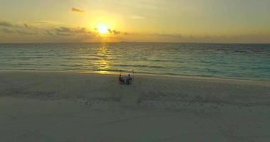 Aerial drone view of a man and woman eating dinner and dining on a tropical island beach. video