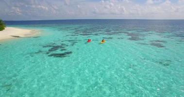 Vista aérea de un dron de una pareja de hombres y mujeres en kayak alrededor de una isla tropical. video
