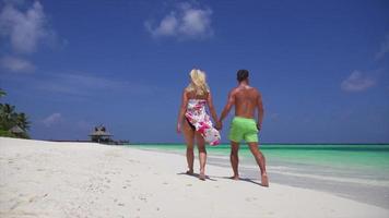 una pareja camina por la playa tomados de la mano en un hotel resort en una isla tropical.