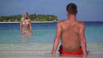 una mujer juguetona salpica agua sobre un hombre en la playa en un hotel resort en una isla tropical. video