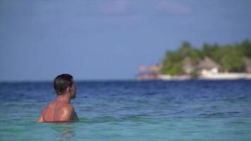 een man komt uit het water op het strand van een resorthotel op een tropisch eiland.
