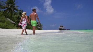 una pareja camina por la playa tomados de la mano en un hotel resort en una isla tropical.