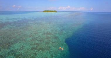 Aerial drone view of a man and woman couple snorkeling over the coral reef of a tropical island. video