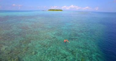 Vista aérea de un dron de una pareja de hombre y mujer buceando sobre el arrecife de coral de una isla tropical.