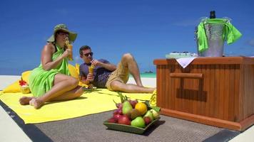 un hombre y una mujer hacen un picnic en la playa de una isla tropical.