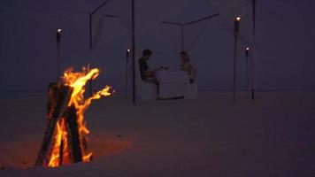 un homme et une femme dînent sur une plage d'une île tropicale avec un feu de camp. video