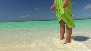 Eine Frau in einem Sarong spaziert am Strand eines Resorthotels auf einer tropischen Insel.