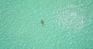 Flygfoto över en kvinna som flyter och simmar på en tropisk ö.