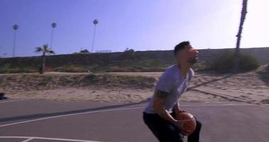 un hombre hace un slam dunk mientras juega baloncesto uno contra uno en una cancha de playa. video
