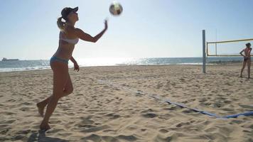 Women players play beach volleyball and a player jump serves an ace serve.