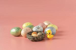 Easter eggs in a natural nest with bird eggs. Painted eggs and a decorative chicken on a pink background of pastel colors. Selective focus photo