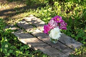 un ramo de grandes peonías blancas y rosas en un frasco de vidrio sobre un puente de madera en el jardín. florecer foto