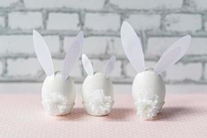Huevos de gallina blanca con orejas de conejo y colas sobre un fondo de pared de ladrillo blanco. una familia. concepto de vacaciones de pascua feliz