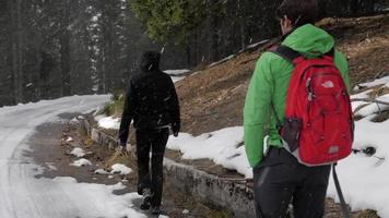 um casal de homem e mulher caminhando enquanto está nevando nas montanhas no inverno.