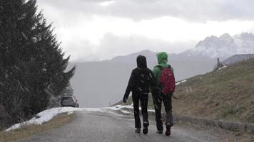 um casal de homem e mulher caminhando enquanto está nevando nas montanhas no inverno.