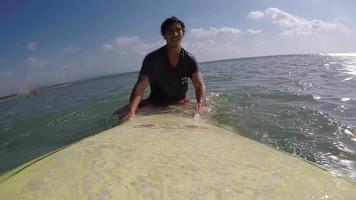 pov van een surfer die peddelt en op golven surft op zijn surfplank.