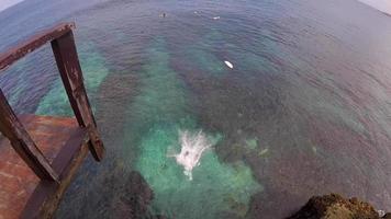 un homme fait un backflip et une falaise sautant dans la mer verte pour aller surfer. video