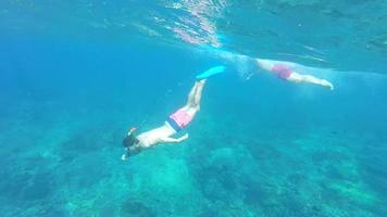 A man and woman couple snorkeling underwater in the blue green sea.