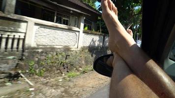 pov de un hombre con los pies fuera de la ventana de un coche en indonesia.