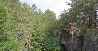 un hombre intenta mantener el equilibrio mientras se relaja en una cuerda floja en las montañas. video