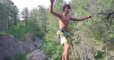 un hombre intenta mantener el equilibrio mientras se relaja en una cuerda floja en las montañas. video
