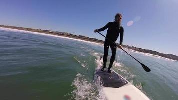 POV of a man sup stand up paddleboard surfing in the whitewash.