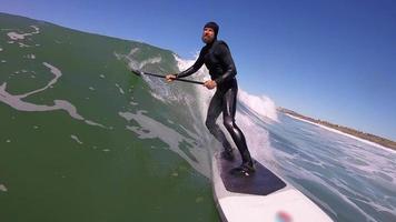 pov de um homem sup stand up paddleboard surf em uma onda.
