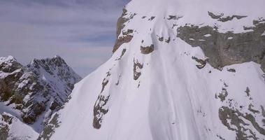 Aerial drone view of a mountain climber skier on the peak summit top of a snow covered mountain. video