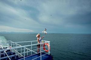 Woman traveling on ferryboat and feeding seagulls flying over the boat from deck, board. photo