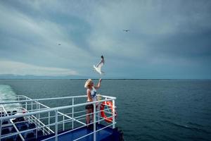 Woman traveling on ferryboat and feeding seagulls flying over the boat from deck, board. photo