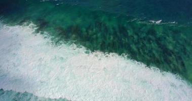 Aerial drone view of the surf and white waves breaking at the beach.
