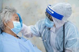 médico asiático con protector facial y traje de ppe nuevo normal para comprobar que el paciente protege la seguridad infección brote de coronavirus covid-19 en la sala de cuarentena del hospital de enfermería. foto