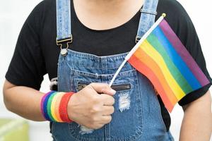 dama asiática con chaqueta de mezclilla azul o camisa de mezclilla y sosteniendo la bandera del color del arco iris, símbolo del mes del orgullo lgbt celebra anualmente en junio las redes sociales de gays, lesbianas, bisexuales, transgénero, derechos humanos. foto