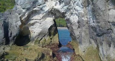 Aerial drone view flying through a natural rock arch the beach. video