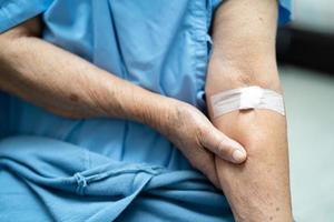 Asian senior or elderly old lady woman patient show cotton wool stop bleeding, after blood drawing testing for annually physical health check up to check cholesterol, blood pressure, and sugar level. photo