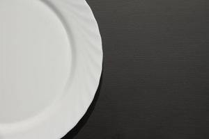 white circle plate on black background, half part of dish blank on matte table, empty place for text photo