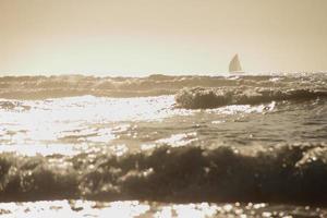 ocean waves under the sunset with shape of sailboat on the horizon photo