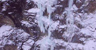 vista aérea do drone de um homem escalando no gelo uma cachoeira congelada nas montanhas. video