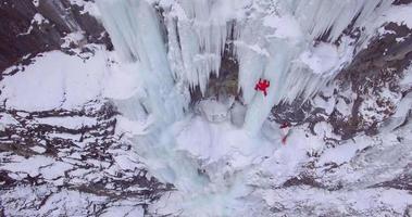 Aerial drone view of a man ice climbing on a frozen waterfall in the mountains.