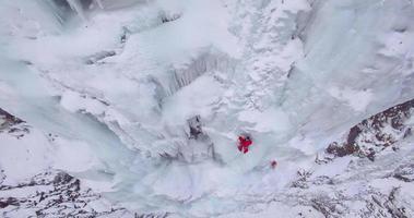 vista aérea do drone de um homem escalando no gelo uma cachoeira congelada nas montanhas. video