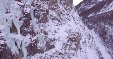Vista aérea de drone de un hombre escalada en hielo en una cascada congelada en las montañas.