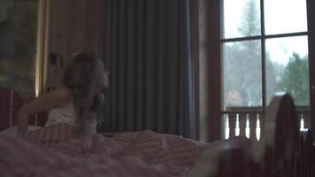 una mujer que se despierta en la cama y mira por la ventana en un hotel de la estación de esquí. video
