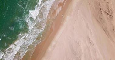 Vista aérea de un vehículo todoterreno 4x4 conduciendo en el viaje de surf en la playa. video