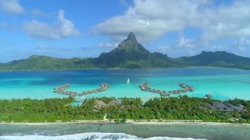 Aerial drone view of a luxury resort, overwater bungalows and sailboat in Bora Bora tropical island.