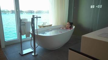 A woman takes a bath in a bathtub bathroom view at a tropical island hotel resort.