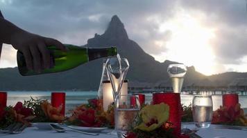 een man die mousserende wijn met champagne schenkt in een resort op een tropisch eiland.