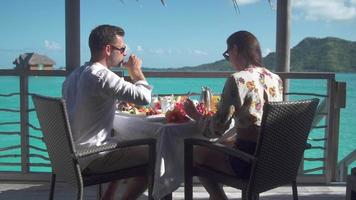 A man and woman couple eating breakfast outside at a tropical island resort.