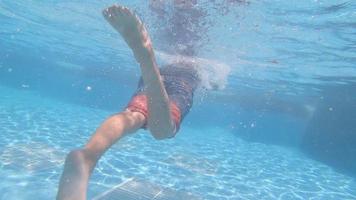 um menino brinca e nada debaixo d'água na piscina de um hotel resort. video