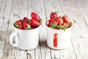 Fresas rojas orgánicas en dos tazas de cerámica blanca sobre fondo de madera rústica. foto