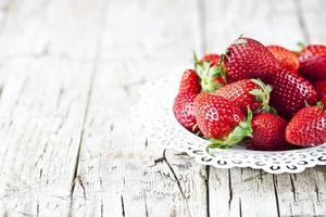 Organic red strawberries on white plate on rustic wooden background. Healthy sweet food, vitamins and fruity concept. photo